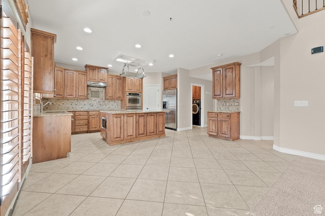 kitchen featuring built in appliances, a center island, light tile patterned flooring, brown cabinets, and decorative backsplash