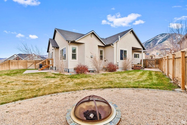 1256 Upland Dr, Tooele, UT 84074 - back of house featuring an outdoor fire pit, a fenced backyard, stucco siding, and a lawn