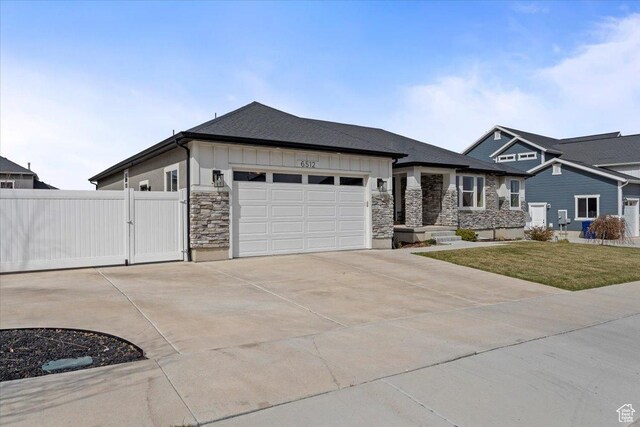 view of front of home with a garage, stone siding, a front lawn, a gate, and driveway