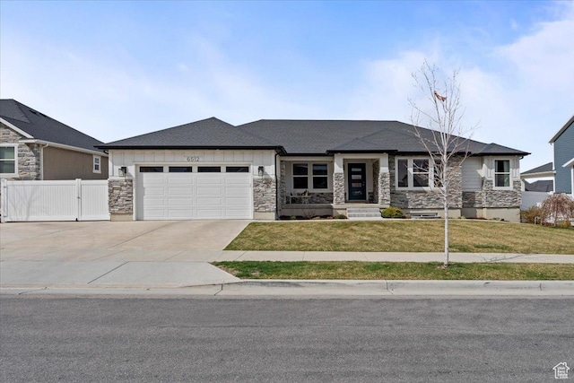 prairie-style house featuring an attached garage, fence, a front yard, and stone siding