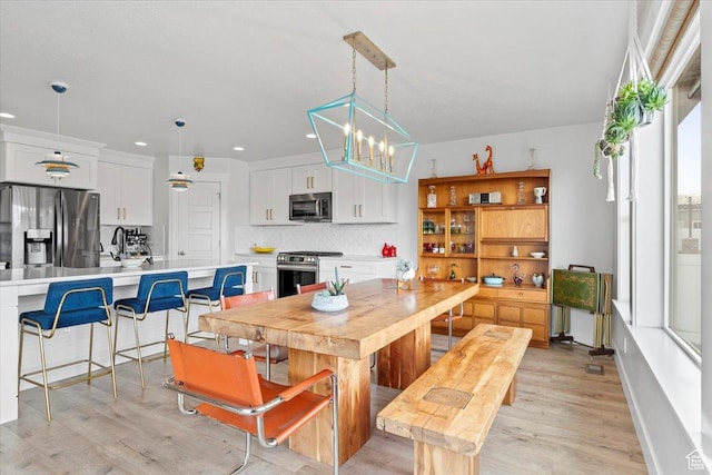 kitchen with tasteful backsplash, light wood-type flooring, white cabinets, light countertops, and stainless steel appliances