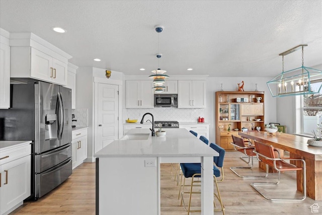 kitchen featuring white cabinets, a sink, light countertops, light wood finished floors, and stainless steel appliances