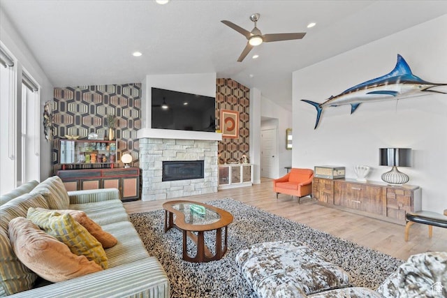 living area featuring a ceiling fan, vaulted ceiling, an accent wall, and wood finished floors