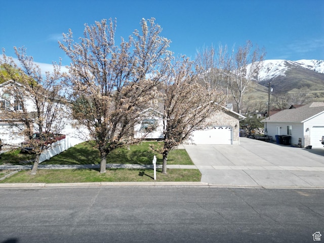 view of property hidden behind natural elements featuring driveway, a mountain view, and an attached garage