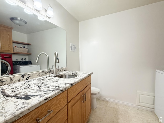 bathroom featuring toilet, washer and clothes dryer, vanity, and baseboards
