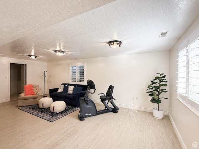 exercise room featuring visible vents, baseboards, a textured ceiling, and wood finished floors