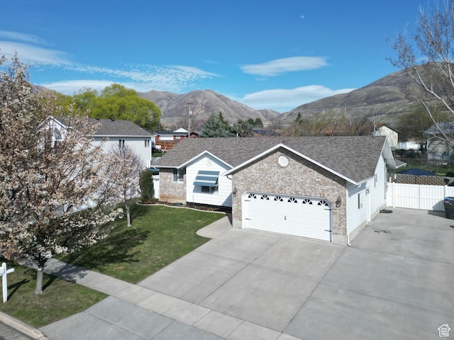 single story home featuring concrete driveway, a mountain view, a front lawn, fence, and a shingled roof