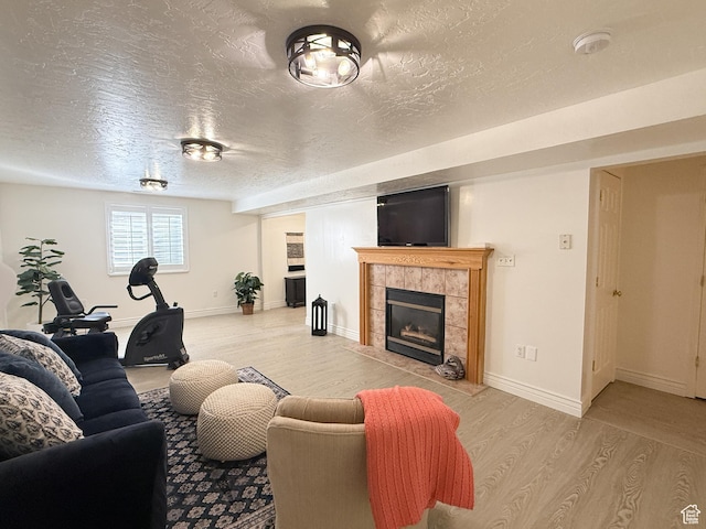 living room with baseboards, light wood finished floors, a tile fireplace, and a textured ceiling