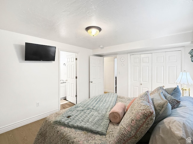 bedroom with a closet, baseboards, ensuite bathroom, a textured ceiling, and wood finished floors