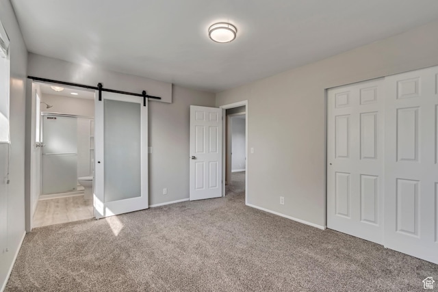 unfurnished bedroom featuring a closet, baseboards, carpet, and a barn door