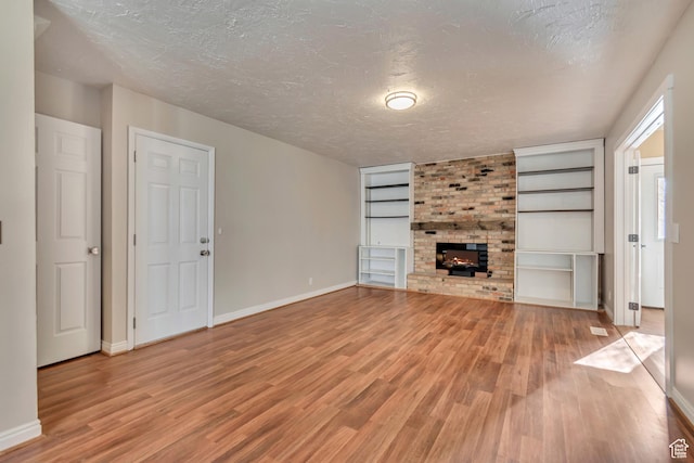 unfurnished living room featuring light wood-style flooring, a textured ceiling, and a brick fireplace