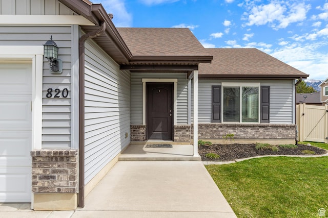 property entrance featuring brick siding, roof with shingles, a gate, and an attached garage