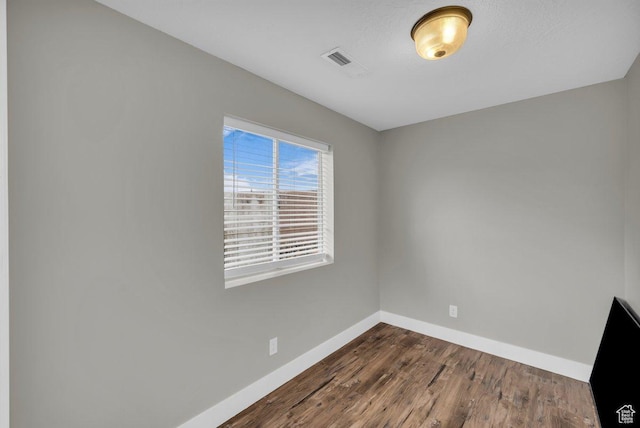 spare room with dark wood-type flooring, visible vents, and baseboards