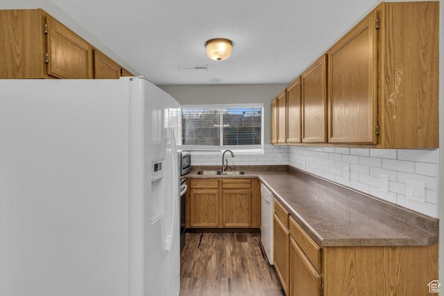 kitchen featuring tasteful backsplash, white appliances, dark wood-type flooring, visible vents, and a sink