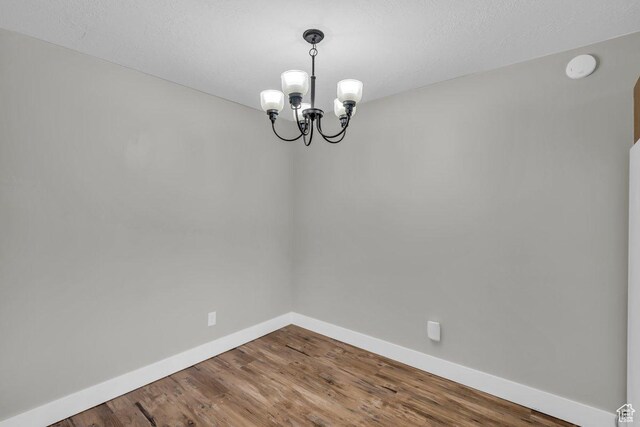 unfurnished dining area with baseboards, an inviting chandelier, wood finished floors, and a textured ceiling
