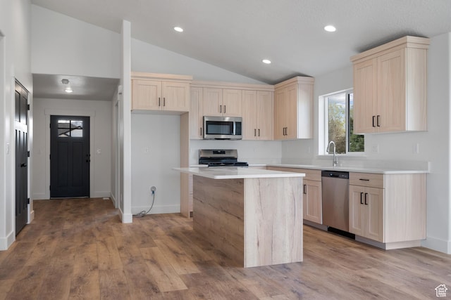 kitchen featuring light brown cabinetry, a center island, appliances with stainless steel finishes, light countertops, and lofted ceiling