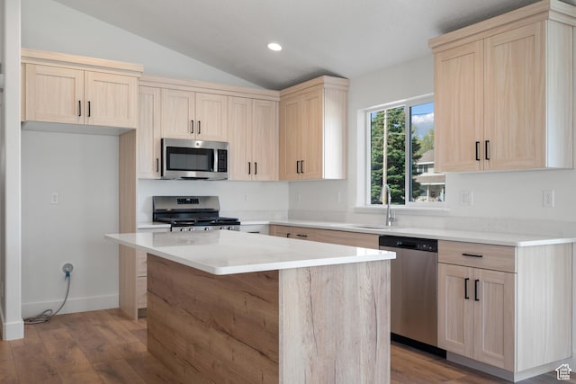 kitchen featuring lofted ceiling, a sink, light brown cabinetry, and appliances with stainless steel finishes