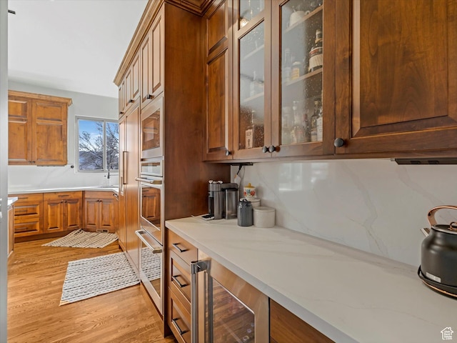 kitchen featuring a sink, brown cabinetry, light wood-type flooring, wine cooler, and glass insert cabinets