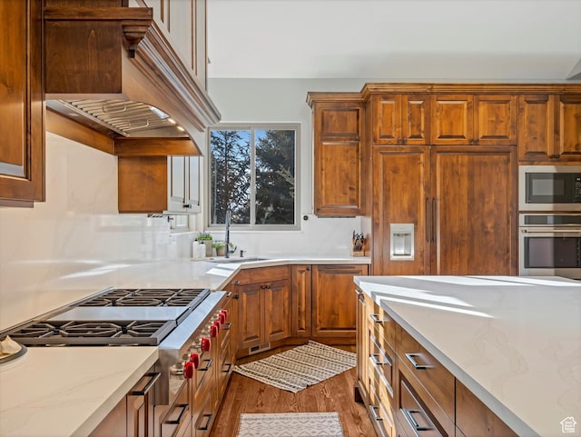 kitchen featuring brown cabinets, custom range hood, a sink, light wood-style flooring, and stainless steel appliances