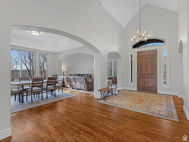 foyer with arched walkways, vaulted ceiling, wood finished floors, baseboards, and a chandelier