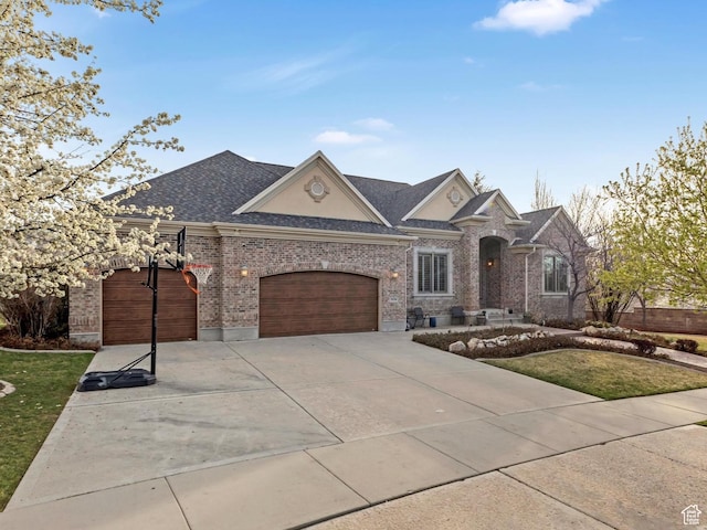 french country style house with roof with shingles, an attached garage, brick siding, driveway, and a front lawn
