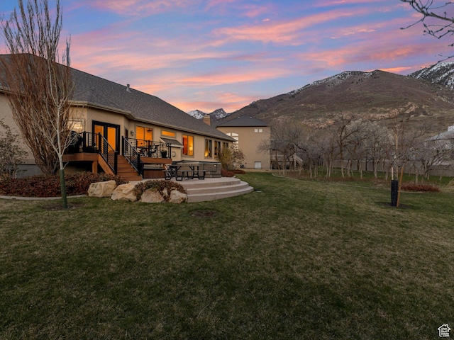 back of house at dusk featuring a lawn, a deck with mountain view, and stucco siding