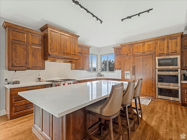 kitchen featuring track lighting, appliances with stainless steel finishes, a center island, and light wood-type flooring