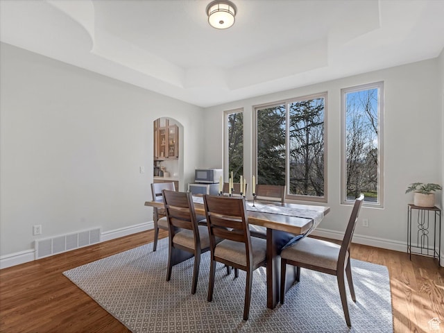 dining area with visible vents, wood finished floors, baseboards, a tray ceiling, and arched walkways