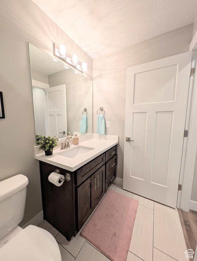 bathroom with toilet, vanity, a textured ceiling, and baseboards