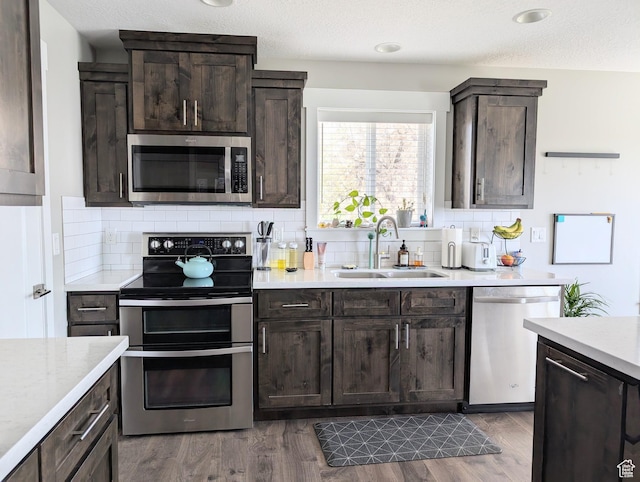 kitchen with dark brown cabinets, stainless steel appliances, light countertops, and a sink