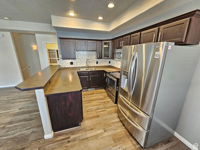 kitchen featuring a sink, dark brown cabinets, stainless steel appliances, backsplash, and light wood-style flooring