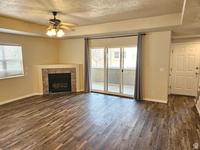 unfurnished living room featuring dark wood-style flooring, a tray ceiling, a wealth of natural light, and a ceiling fan