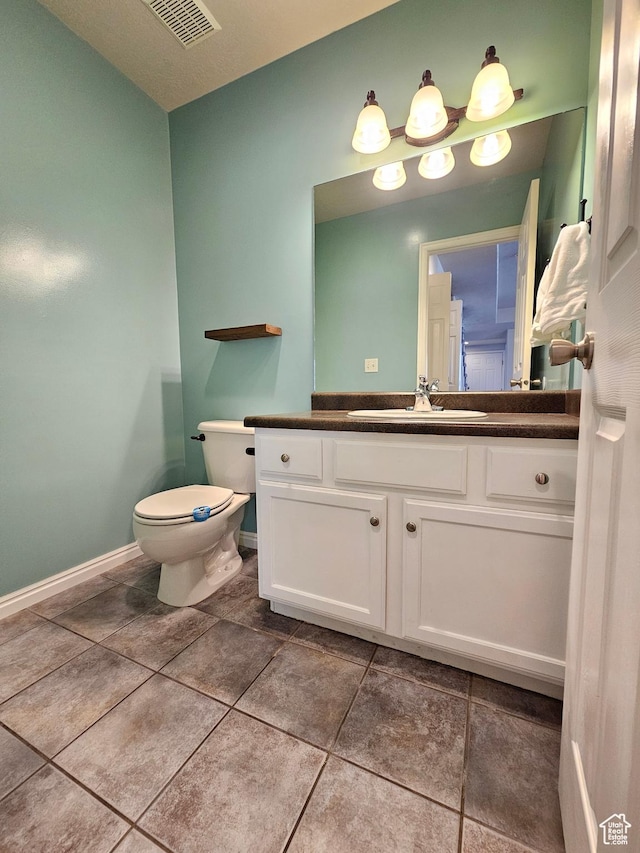 half bath with visible vents, baseboards, toilet, vanity, and tile patterned floors