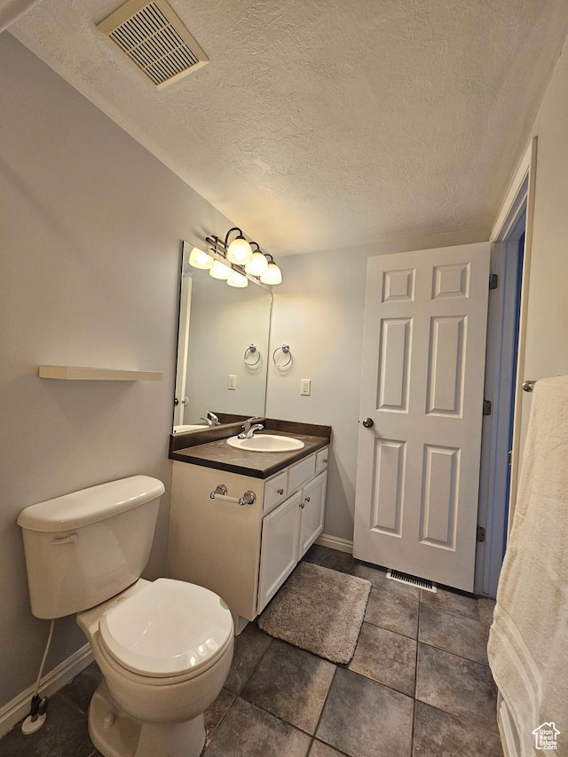 bathroom with vanity, baseboards, a textured ceiling, toilet, and visible vents