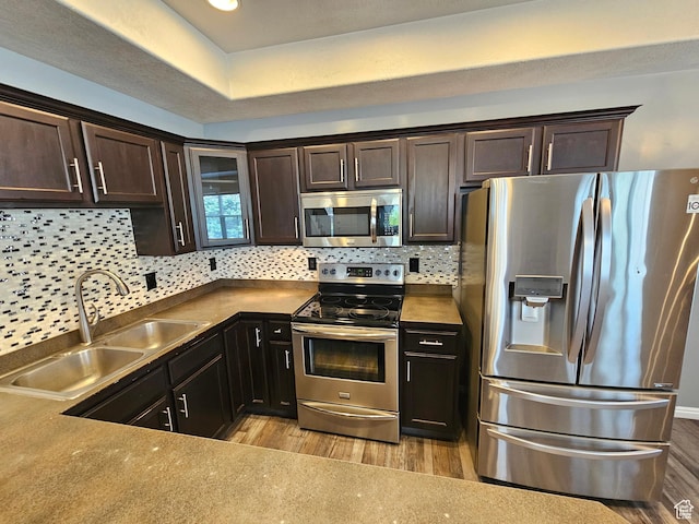 kitchen with tasteful backsplash, dark brown cabinetry, appliances with stainless steel finishes, light wood finished floors, and a sink