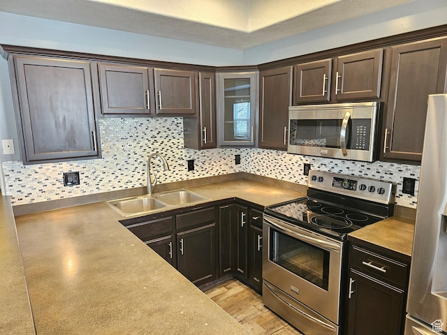 kitchen featuring decorative backsplash, dark brown cabinets, a sink, stainless steel appliances, and light wood finished floors