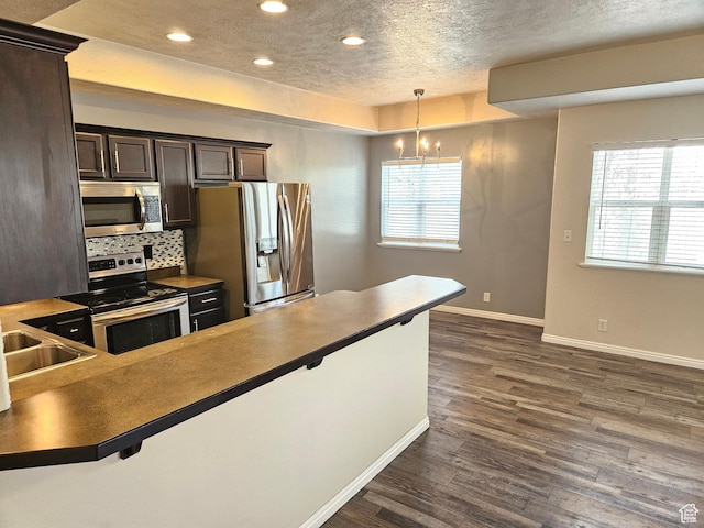 kitchen featuring a healthy amount of sunlight, dark countertops, a sink, stainless steel appliances, and dark wood-style floors