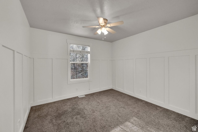 spare room featuring dark carpet, a decorative wall, and a ceiling fan