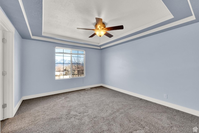 carpeted empty room featuring a raised ceiling, ceiling fan, and baseboards