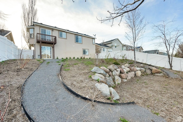 back of house featuring a balcony, stucco siding, and a fenced backyard
