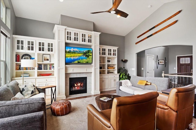 living area featuring high vaulted ceiling, arched walkways, a tiled fireplace, and a ceiling fan