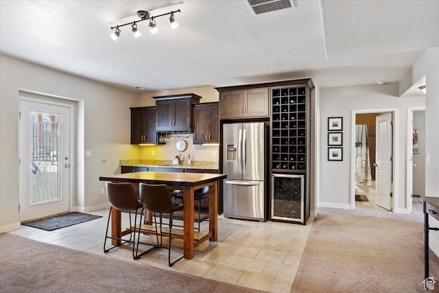 kitchen featuring dark brown cabinetry, light carpet, stainless steel refrigerator with ice dispenser, visible vents, and wine cooler