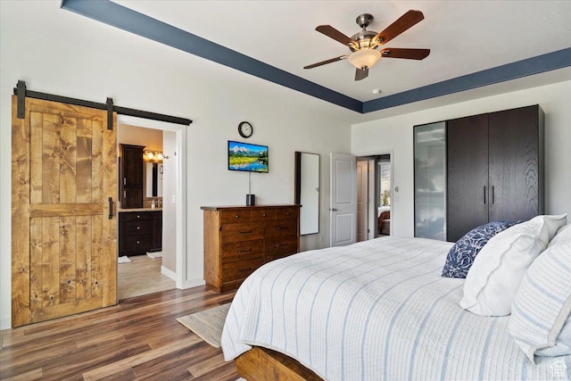 bedroom featuring a ceiling fan, a barn door, wood finished floors, a raised ceiling, and baseboards