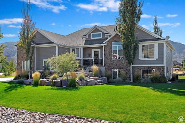 back of property with a yard, stone siding, a mountain view, and a shingled roof