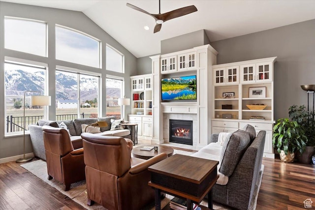 living room featuring ceiling fan, a fireplace, high vaulted ceiling, wood finished floors, and baseboards