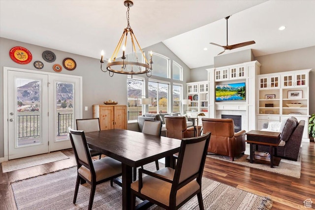 dining room featuring a glass covered fireplace, recessed lighting, high vaulted ceiling, ceiling fan with notable chandelier, and wood finished floors