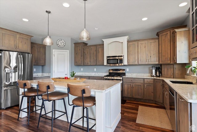 kitchen with appliances with stainless steel finishes, a breakfast bar, a center island, dark wood finished floors, and a sink