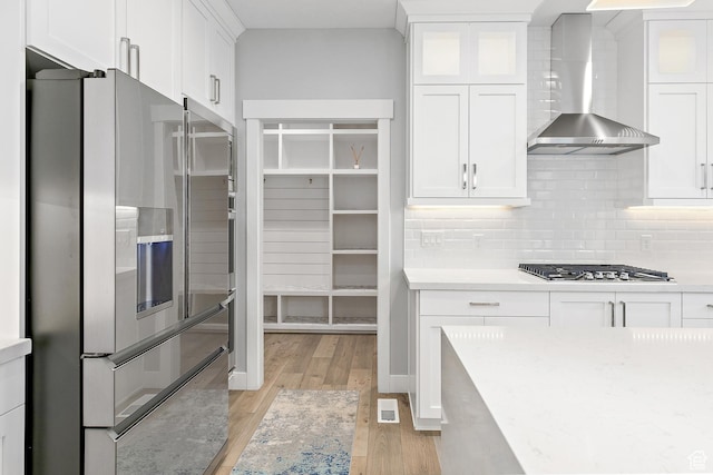 2913 S Puddle Ln, Saratoga Springs, UT 84045 - kitchen with light wood-type flooring, backsplash, white cabinetry, wall chimney range hood, and appliances with stainless steel finishes