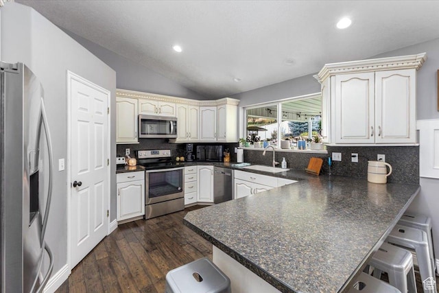 kitchen featuring a sink, dark countertops, appliances with stainless steel finishes, a peninsula, and vaulted ceiling
