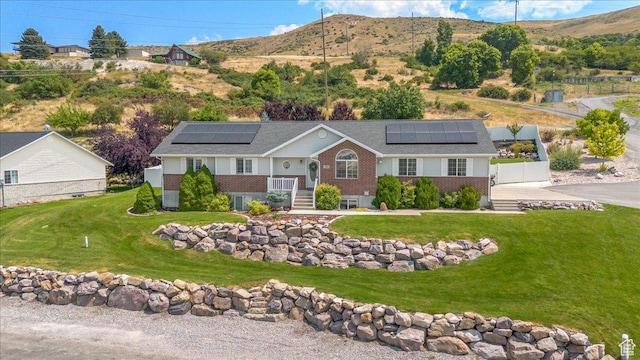 view of front of property featuring a mountain view, solar panels, a front lawn, and brick siding